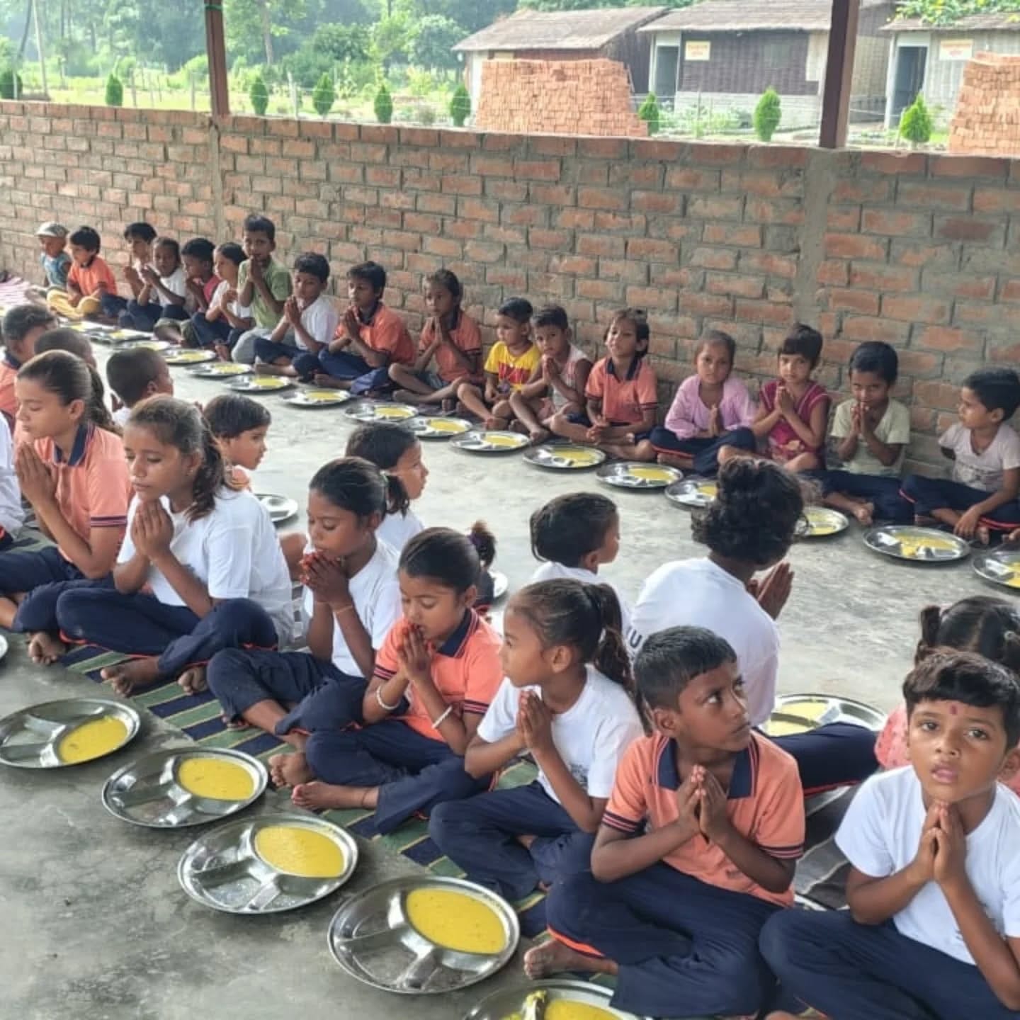 Children seated in long rows with their hands together before a meal