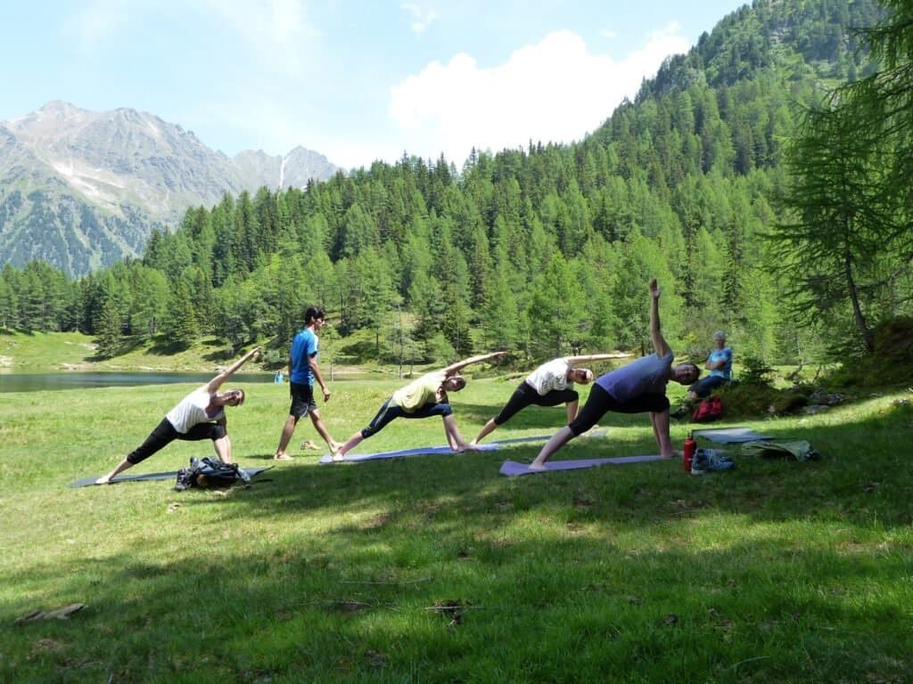 Group yoga practice on a meadow surrounded by forested mountains