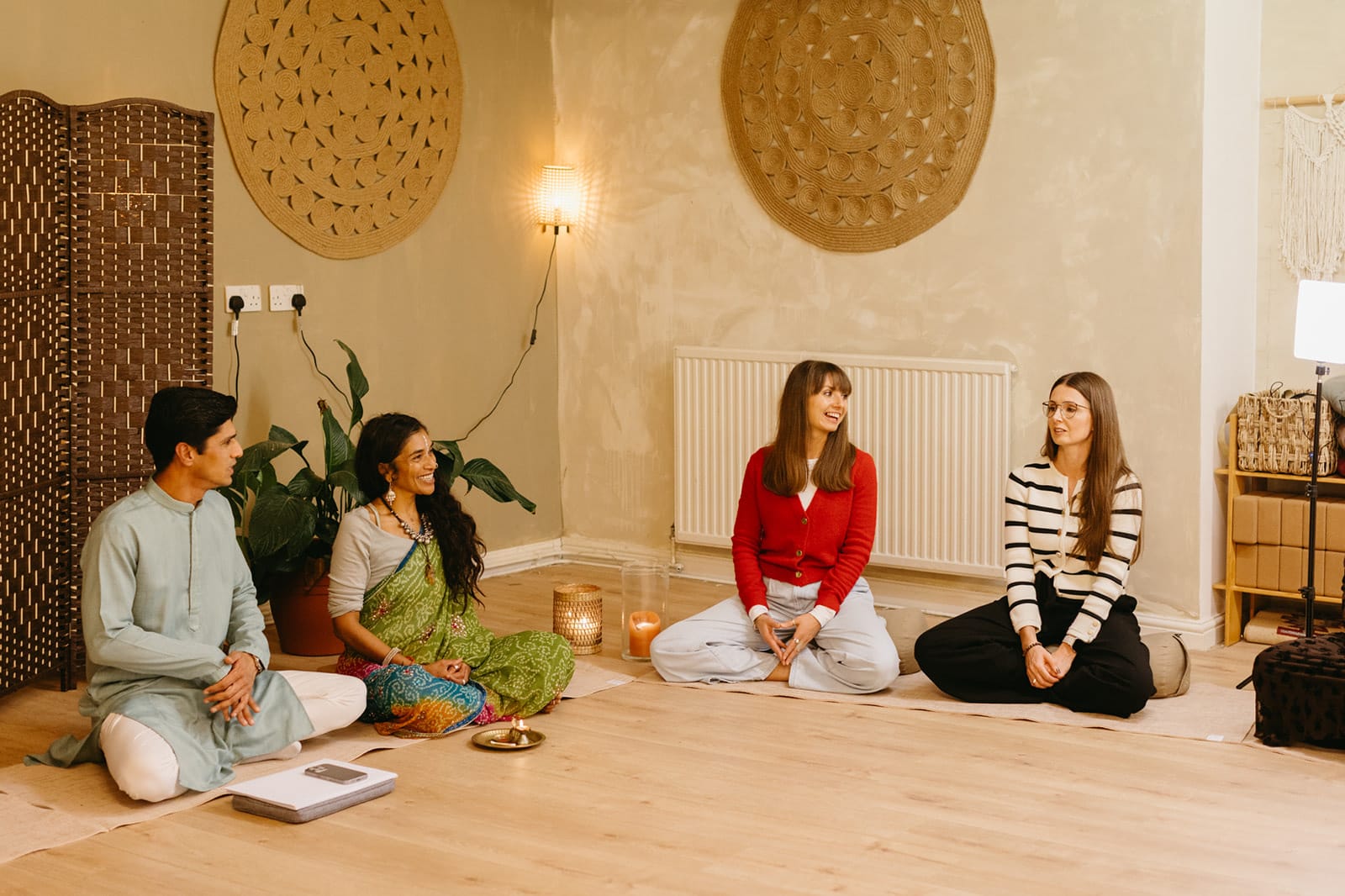 Teachers and trainees seated together in a circle beneath woven wall hangings