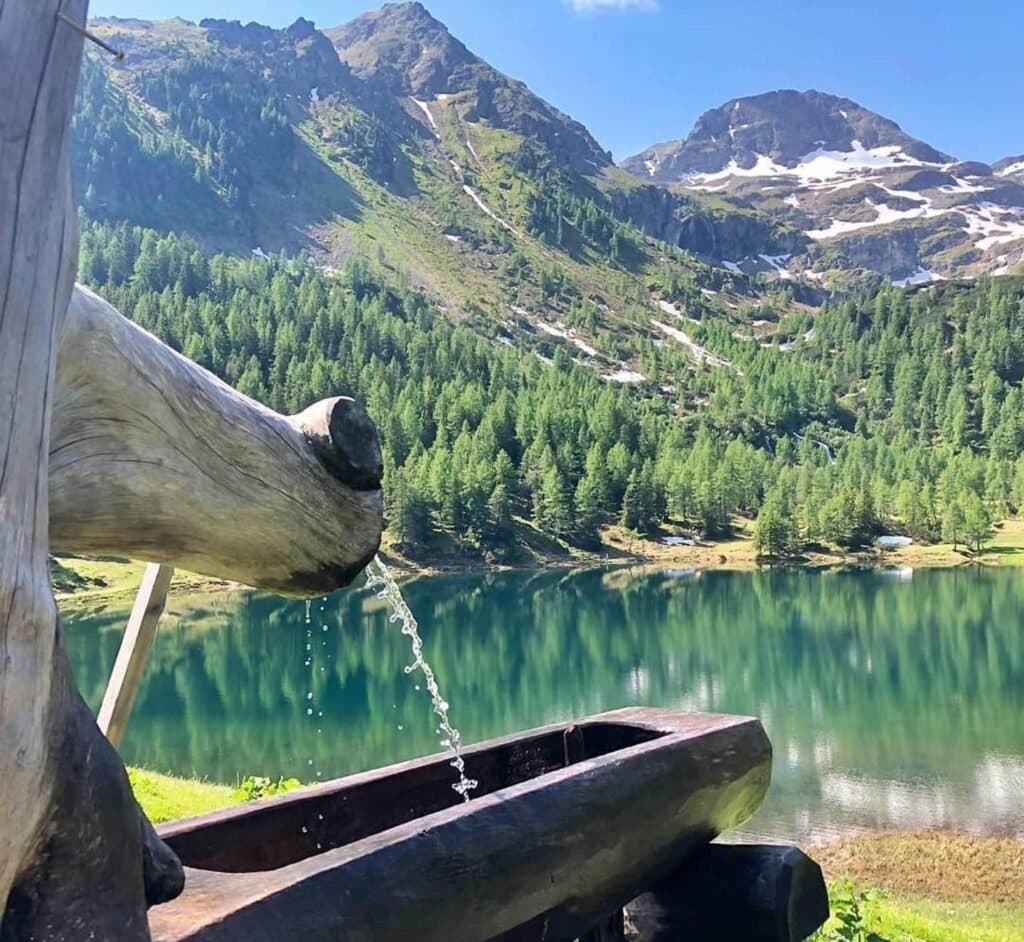 A carved wooden fountain overlooking an alpine lake and mountains