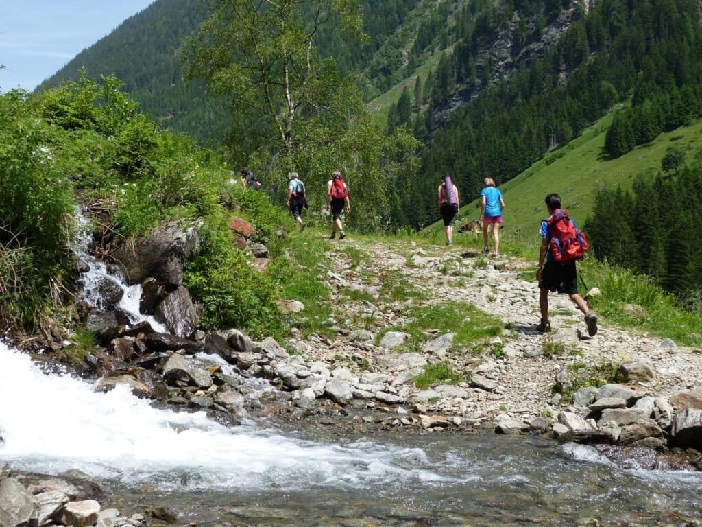 Hikers walking a rocky trail beside a mountain stream
