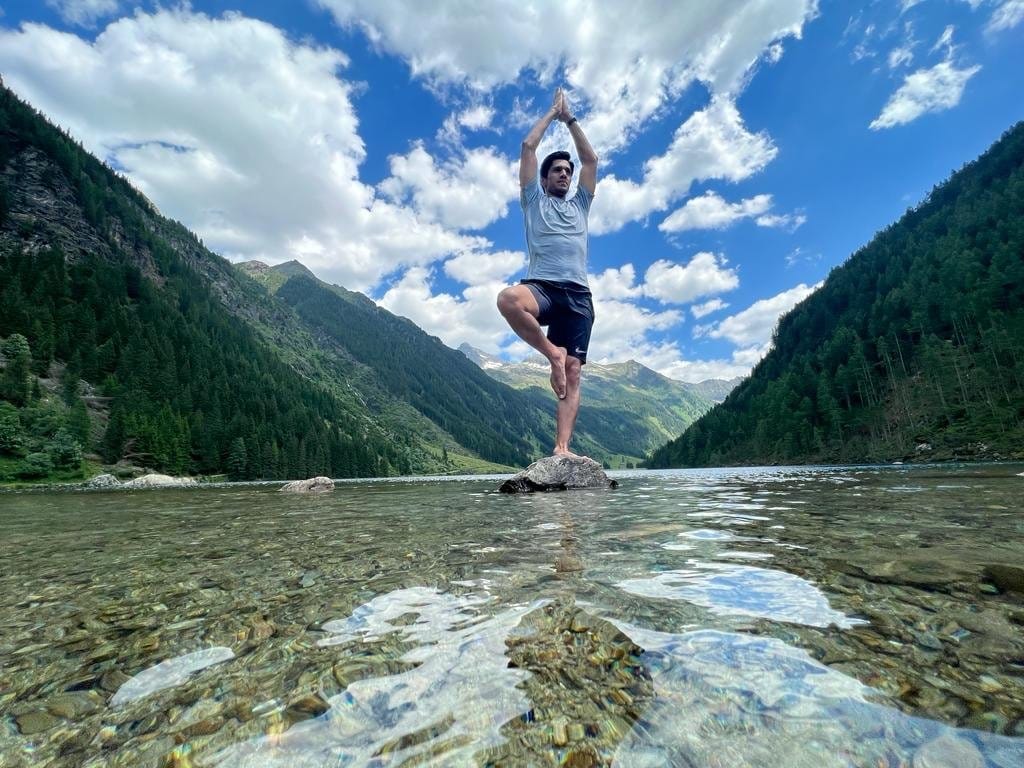 A man balancing in tree pose on a rock in a clear alpine lake