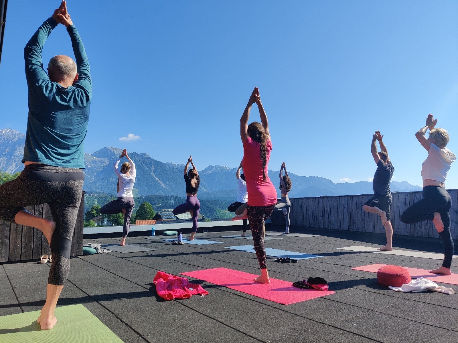 Retreat guests balancing in tree pose on the rooftop terrace with the Alps behind