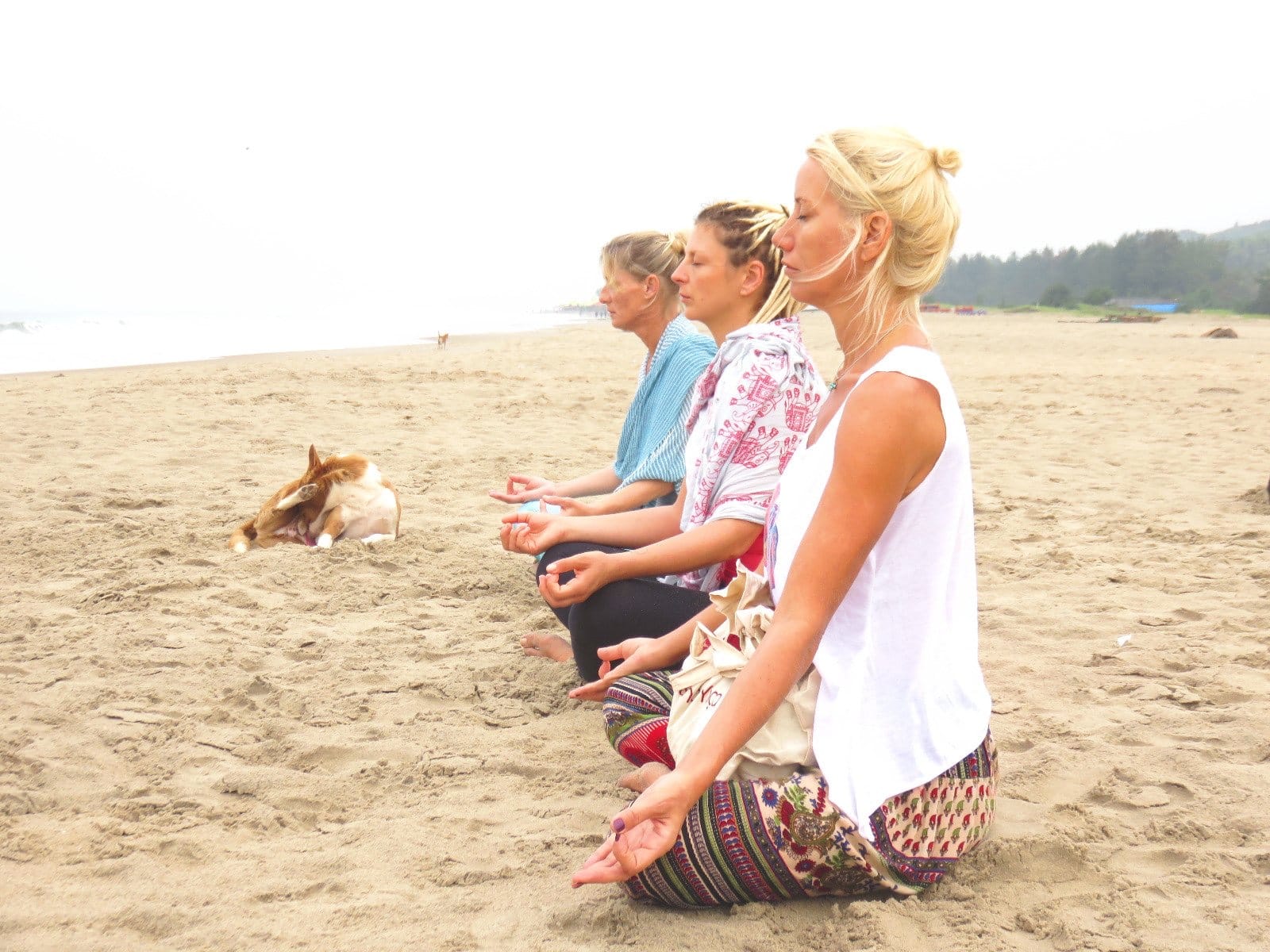 Three women meditating cross-legged on the sand