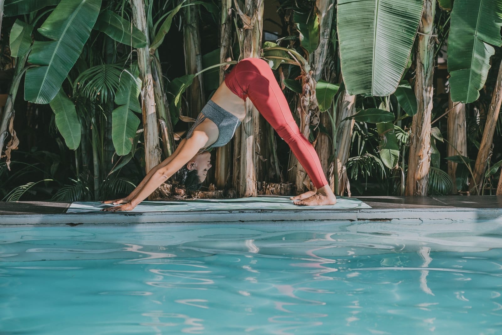 A woman in downward-facing dog beside a pool framed by banana palms